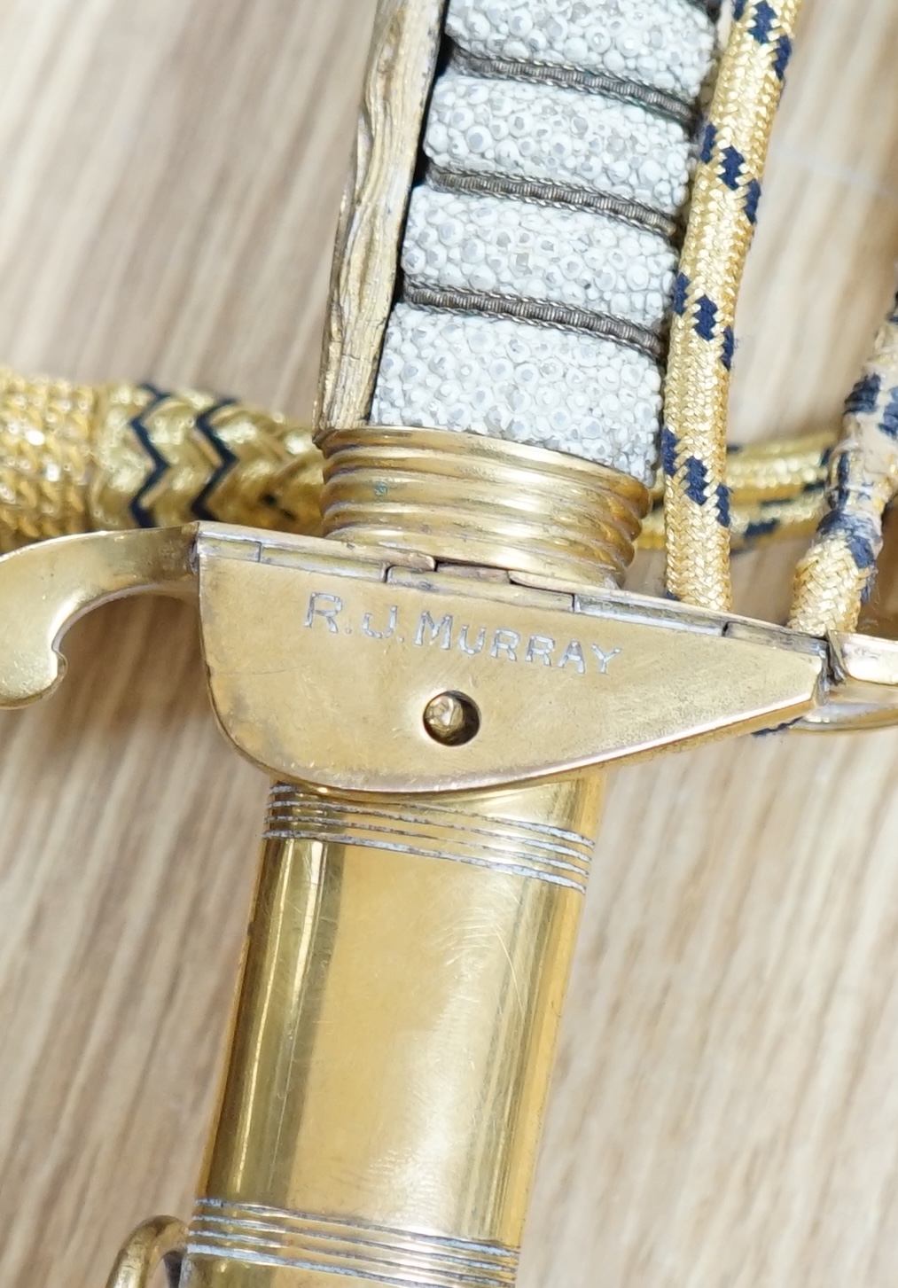 A Victorian Royal Navy officer’s sword by Grieves, engraved blade, lion’s head pommel, fish skin grip, folding guard engraved with R.J. Murray, with its sword knot and leather scabbard with brass mounts, blade 79cm. Cond